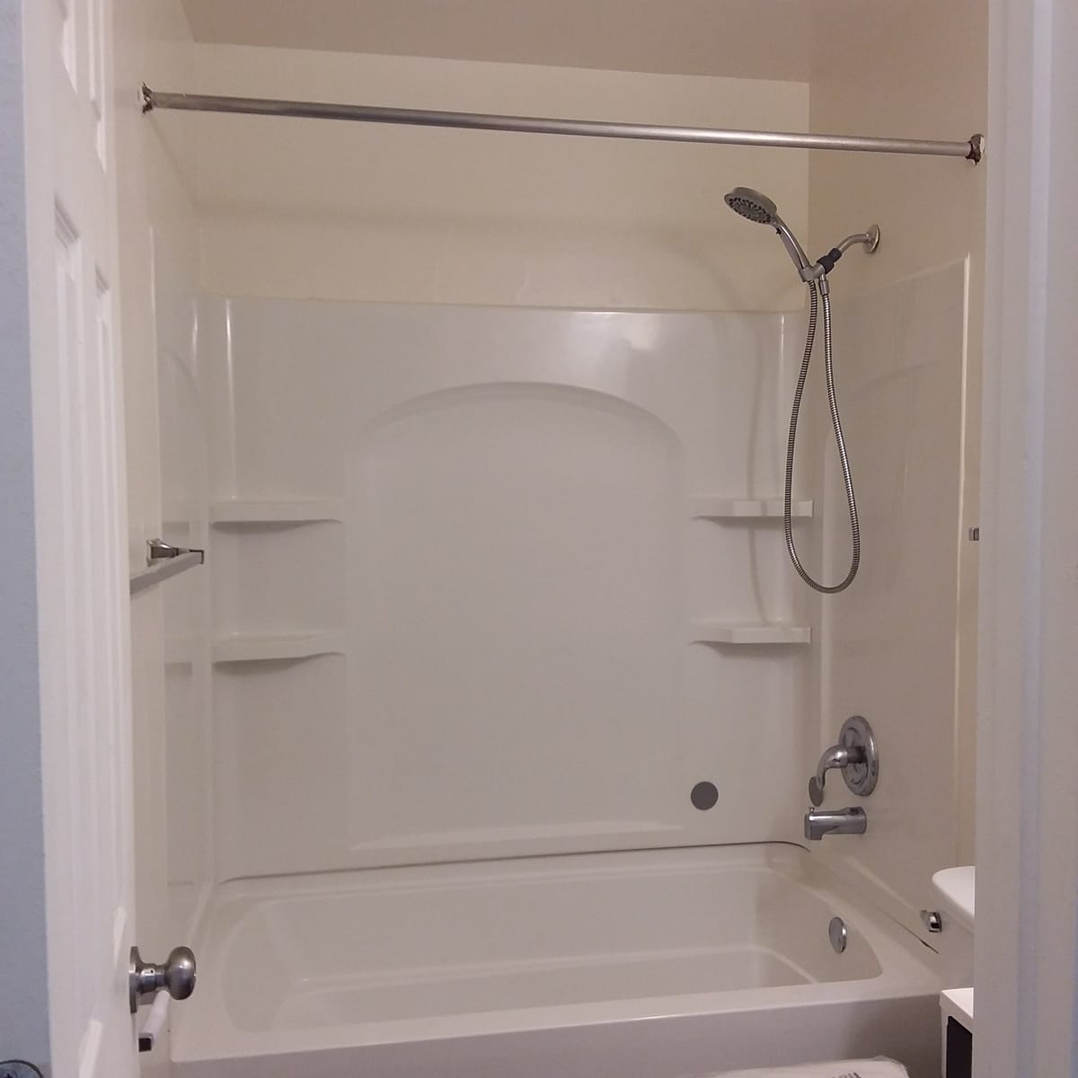 A white tub and shower surround at Indian Head Village with built-in shelves, a handheld shower head, and a curtain rod