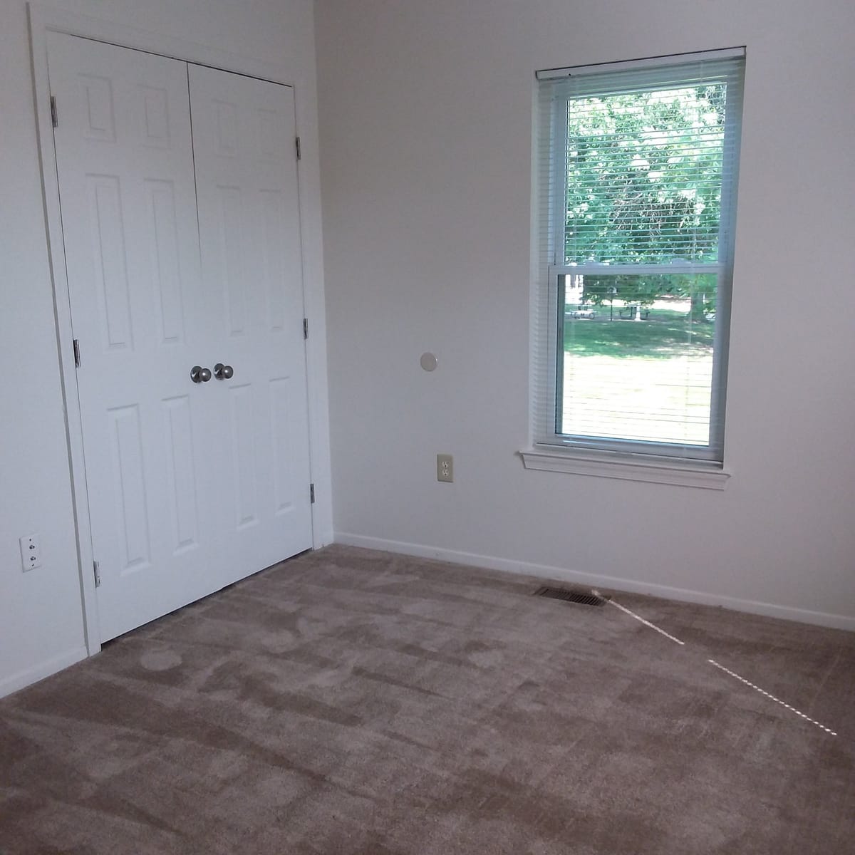 A carpeted bedroom at Indian Head Village with a double-door closet and a window looking out to a lawn and trees