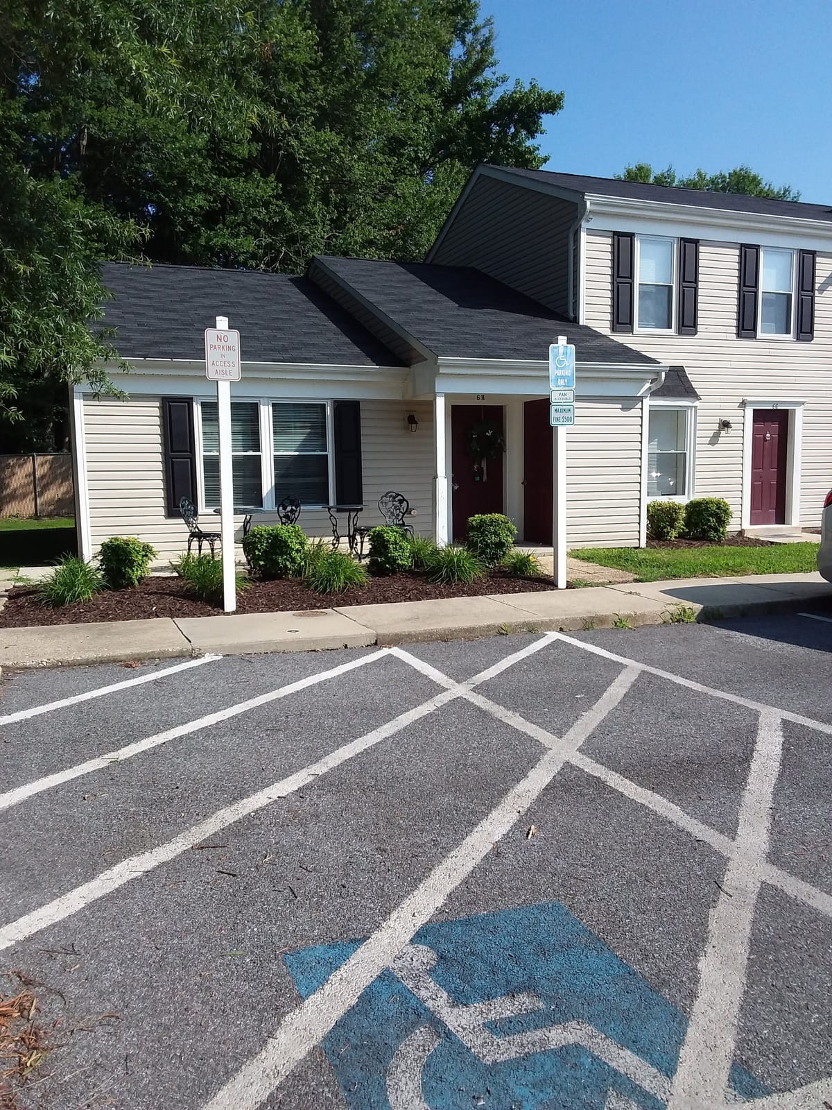 A townhouse entrance at Indian Head Village with a covered stoop, a bay window, and a small table and chairs on the walk beside a mulched garden bed