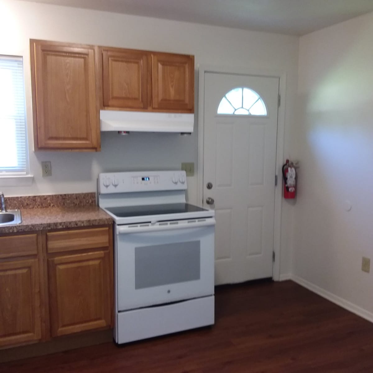 The kitchen at Indian Head Village from another angle, with a white electric range and range hood, oak cabinets, and a back door with a fan-shaped window